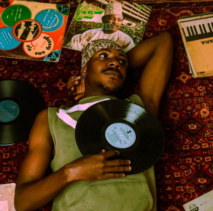 A young man lies on a patterned rug surrounded by vinyl records, embracing a nostalgic musical ambiance.